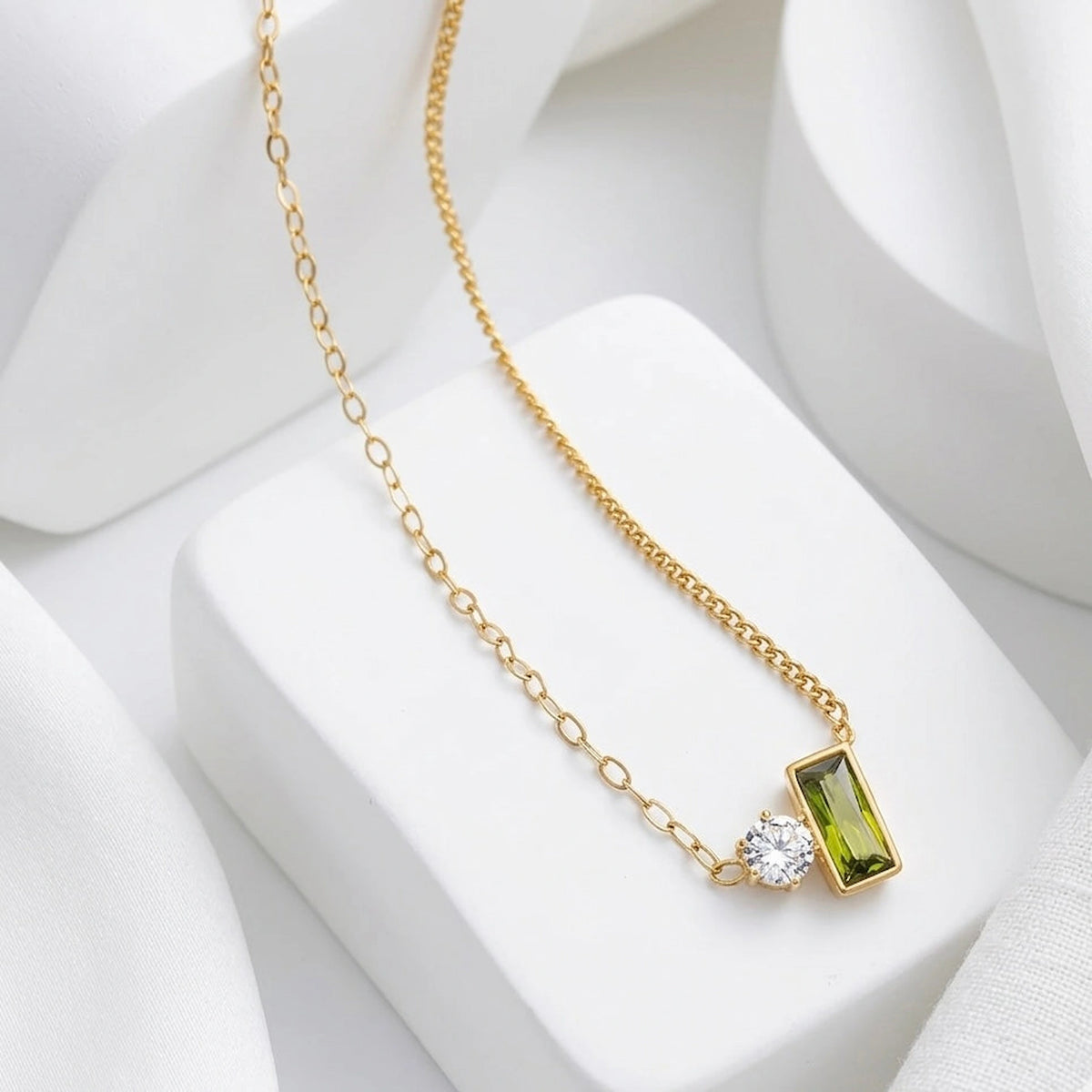 BEHI MILANO Ilona Necklace — gold green gemstone pendant displayed on white architectural podium