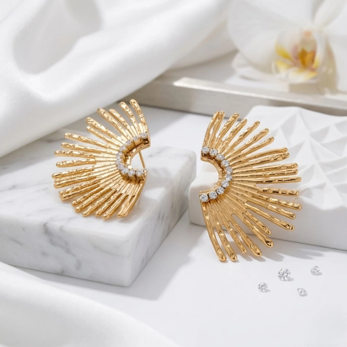 BEHI MILANO Indigamond Earrings — gold sunburst fan studs on white marble in warm sunlight