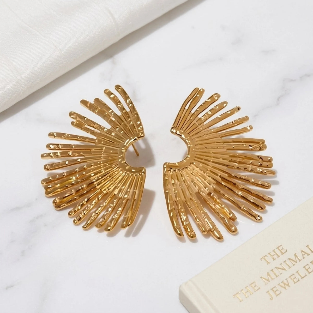 BEHI MILANO Indigo Earrings — pair of gold fan statement earrings on white marble backdrop