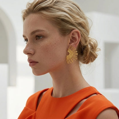 BEHI MILANO Indigo Earrings — blonde model wearing gold sunburst fan statement earrings in profile with orange top