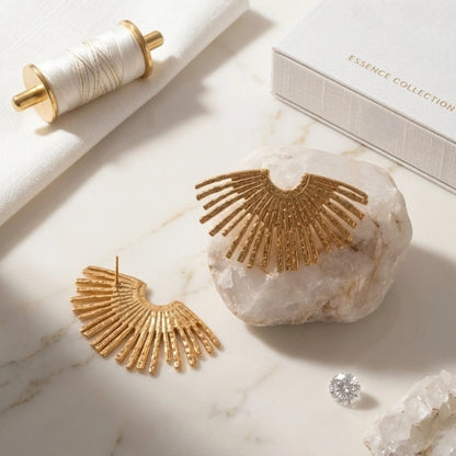 BEHI MILANO Indigo Earrings — gold sunburst fan studs displayed on white marble surface with thread spool