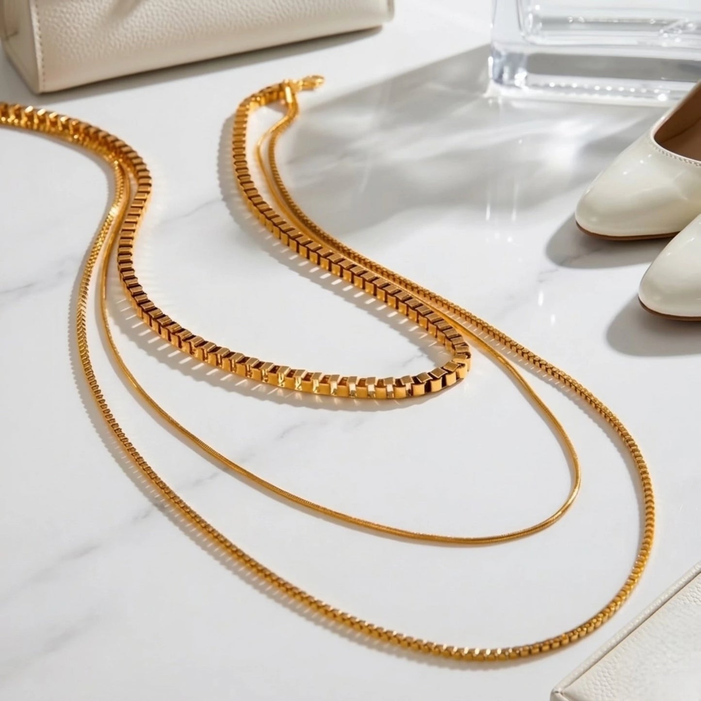 BEHI MILANO Ira Necklace — triple layered gold necklace laid flat on white marble next to high heels