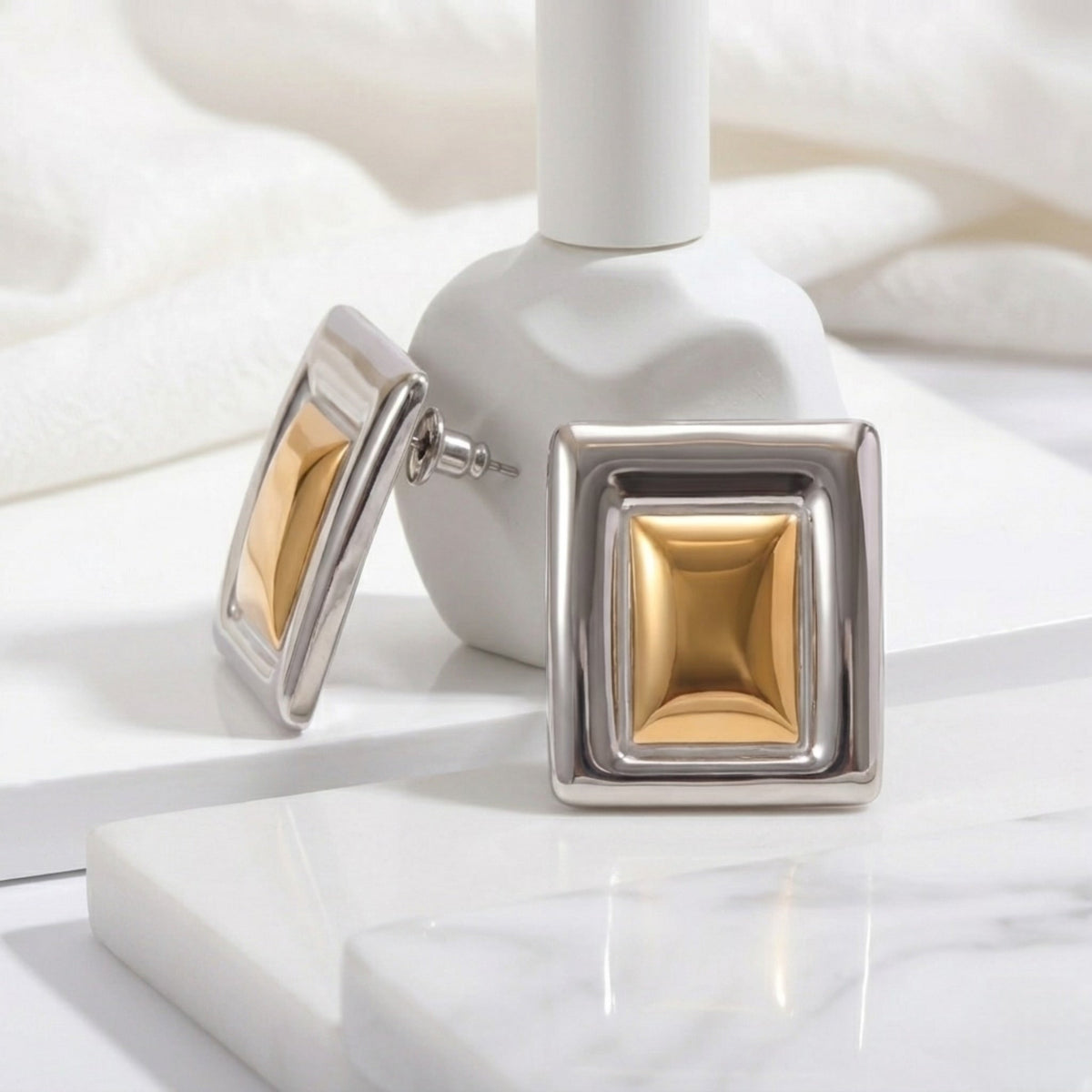 BEHI MILANO Isabella Earrings — close up of two tone geometric studs mounted on white ceramic display stand