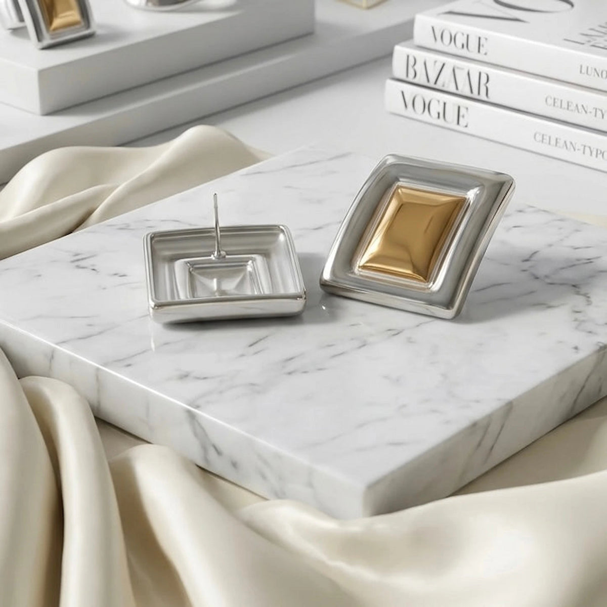 BEHI MILANO Isabella Earrings — two tone statement studs flat lay on white silk and fashion magazines