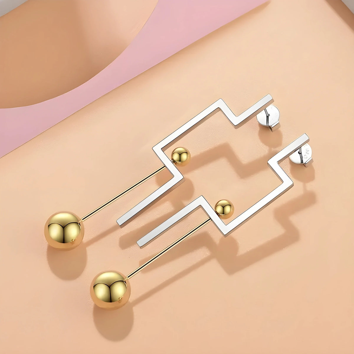 BEHI MILANO Isidora Earrings — flat lay display of two tone gold and silver linear earrings on peach surface