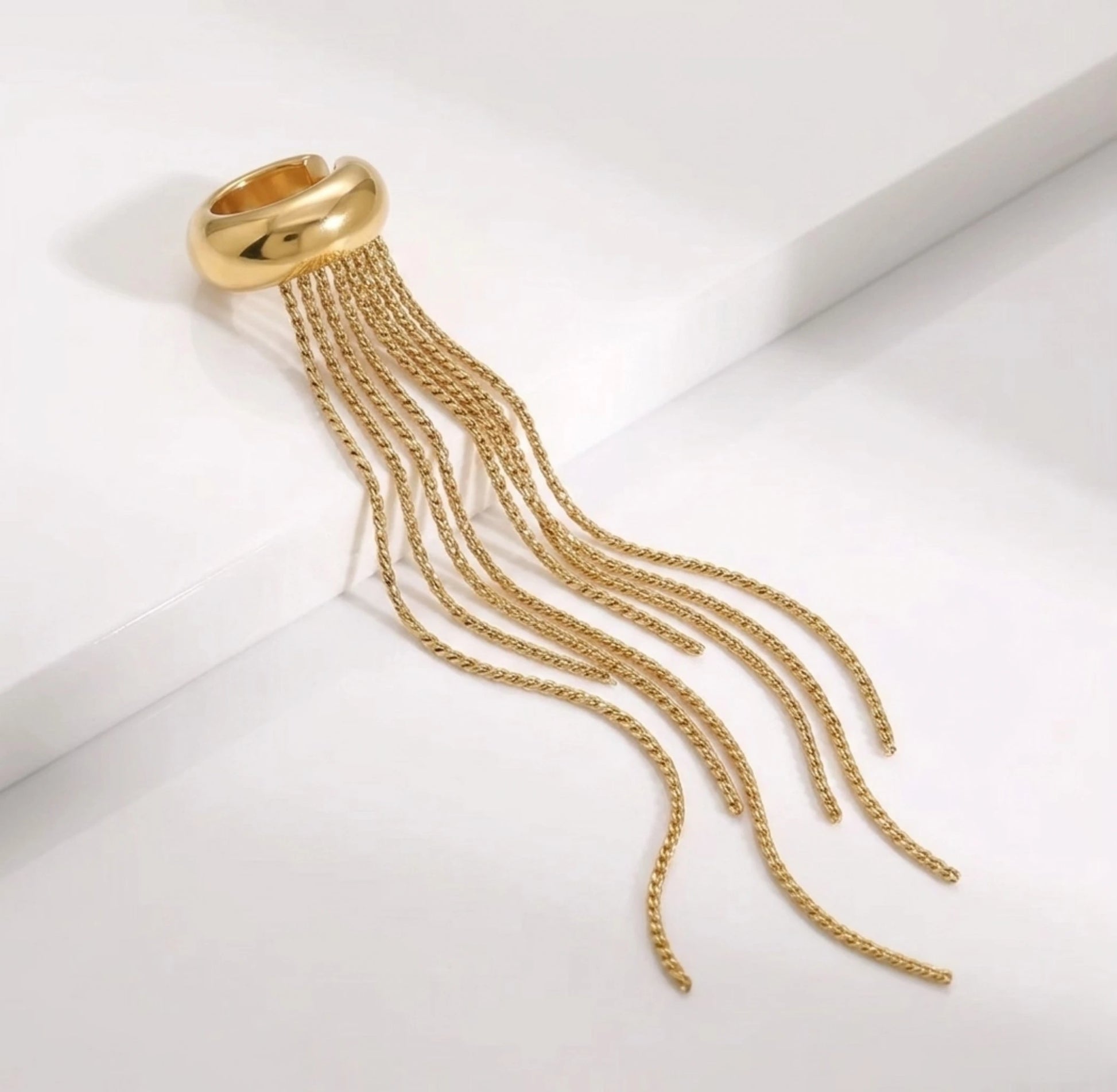 BEHI MILANO Iskra Ear Cuff — gold cascading fringe cuff resting on smooth curved pedestal