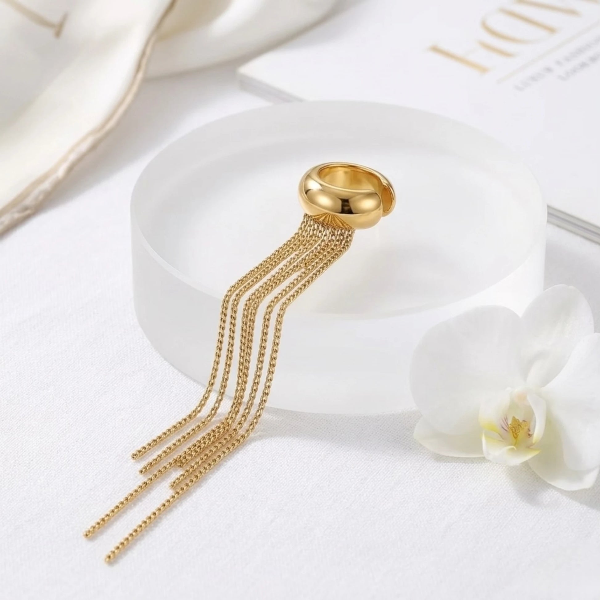 BEHI MILANO Iskra Ear Cuff — 18k gold fringe ear cuff displayed next to white orchid flower