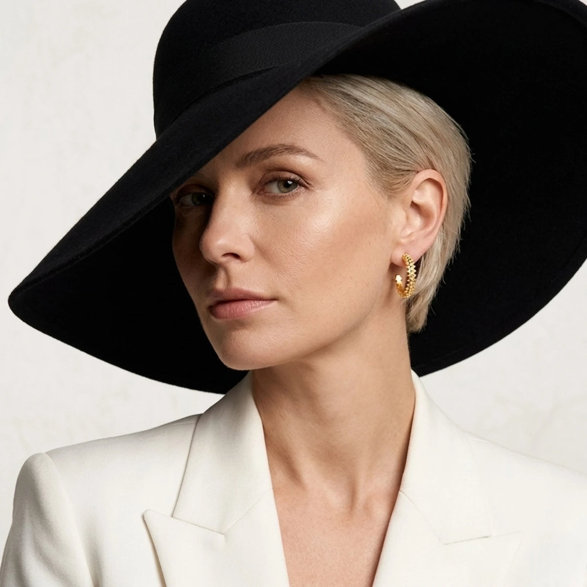 BEHI MILANO Isla Earrings — frontal portrait of model in black fedora hat wearing 18k gold pyramid hoops