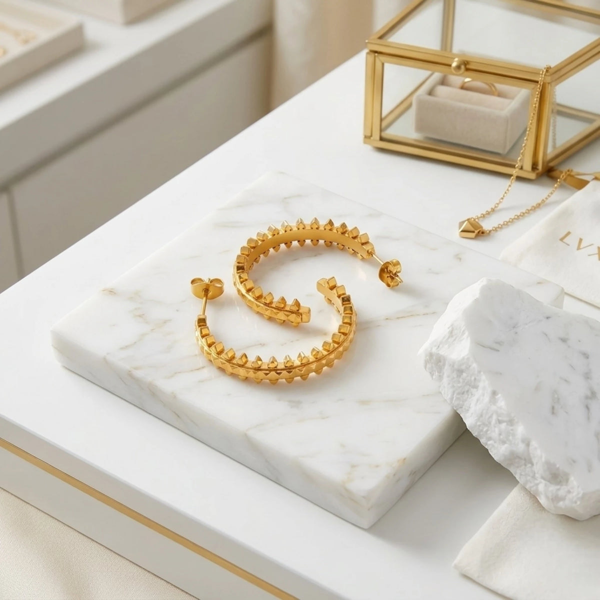 BEHI MILANO Isla Earrings — gold pyramid open hoops on white marble slab with luxury jewelry box