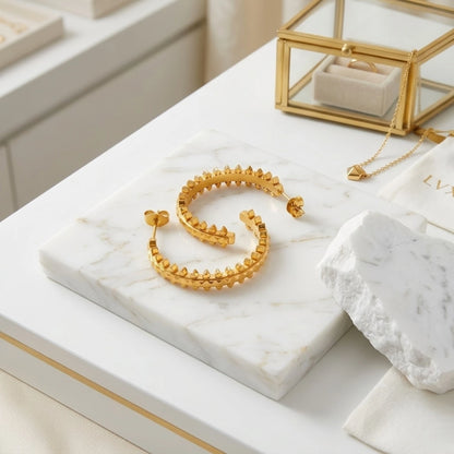 BEHI MILANO Isla Earrings — gold pyramid open hoops on white marble slab with luxury jewelry box