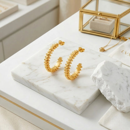 BEHI MILANO Isla Earrings — close up detail display of gold pyramid textured hoops on white marble