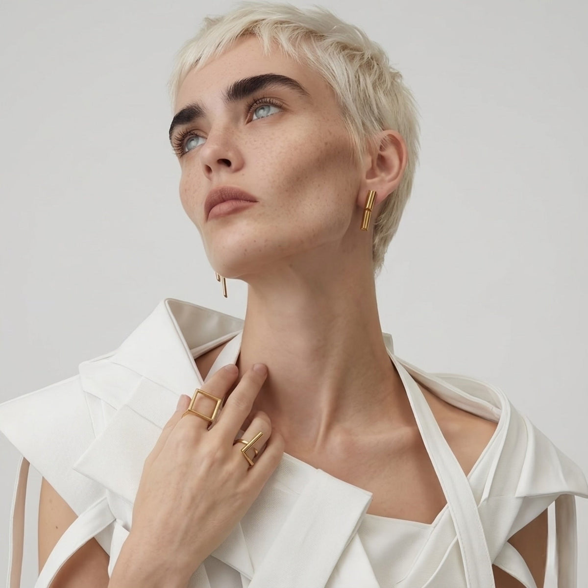 BEHI MILANO Ivana Earrings — blonde model in white top wearing gold architectural dual bar drop earrings