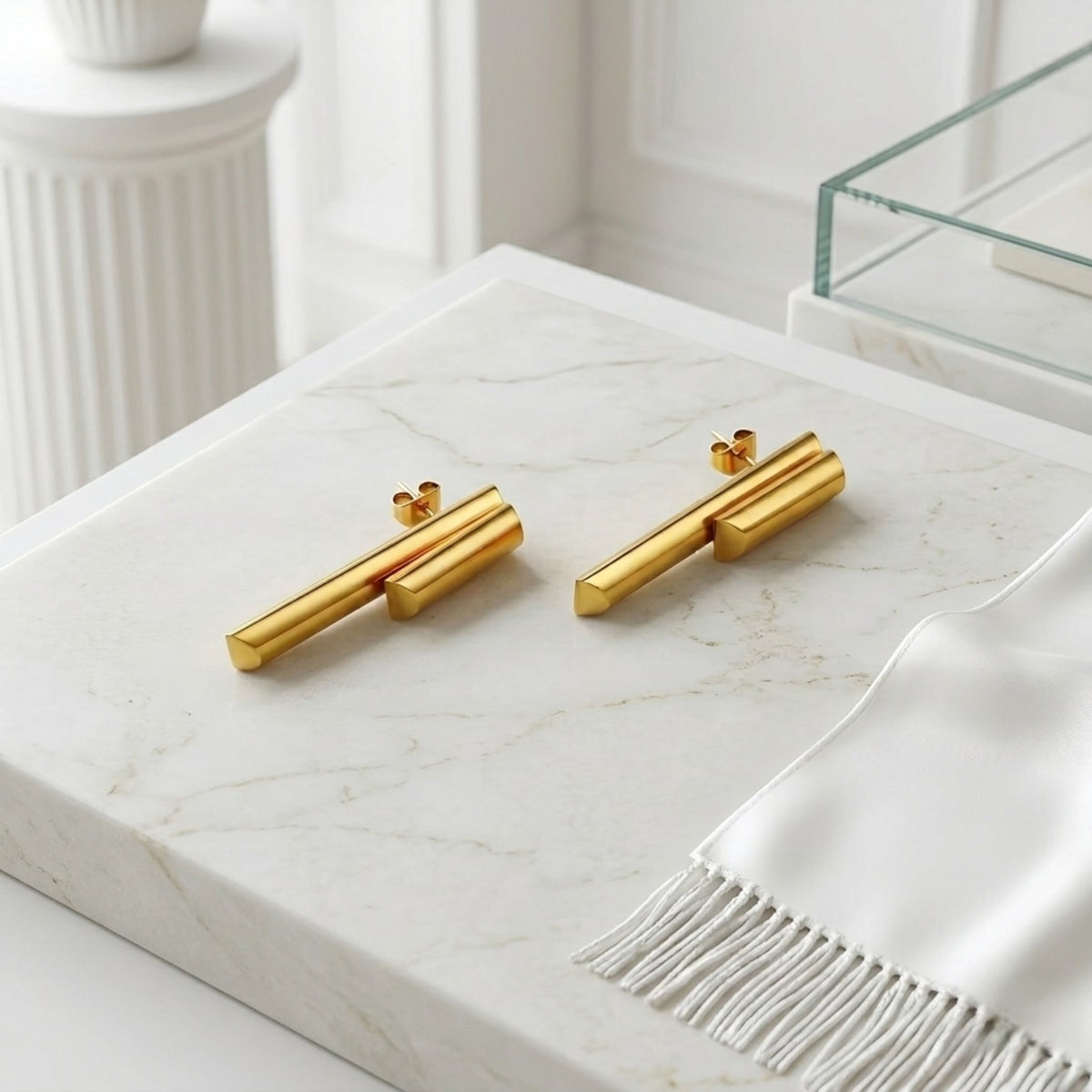 BEHI MILANO Ivana Earrings — 18k gold geometric drop studs resting on marble slab with linen