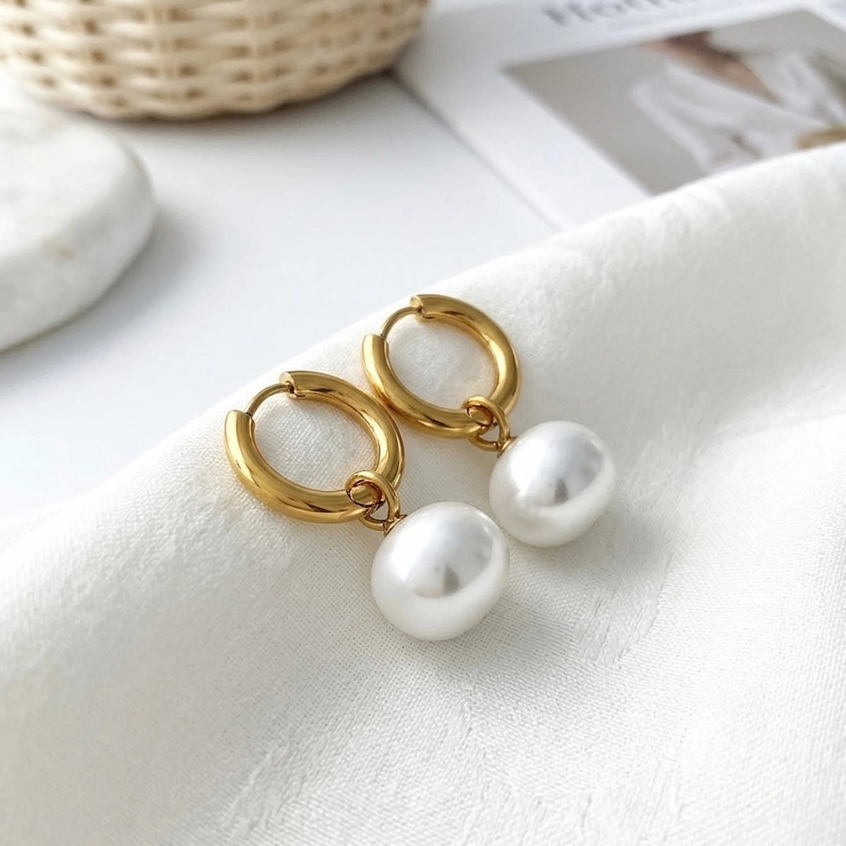 BEHI MILANO Jade Earrings — gold pearl drop hoops on white satin fabric with basket backdrop