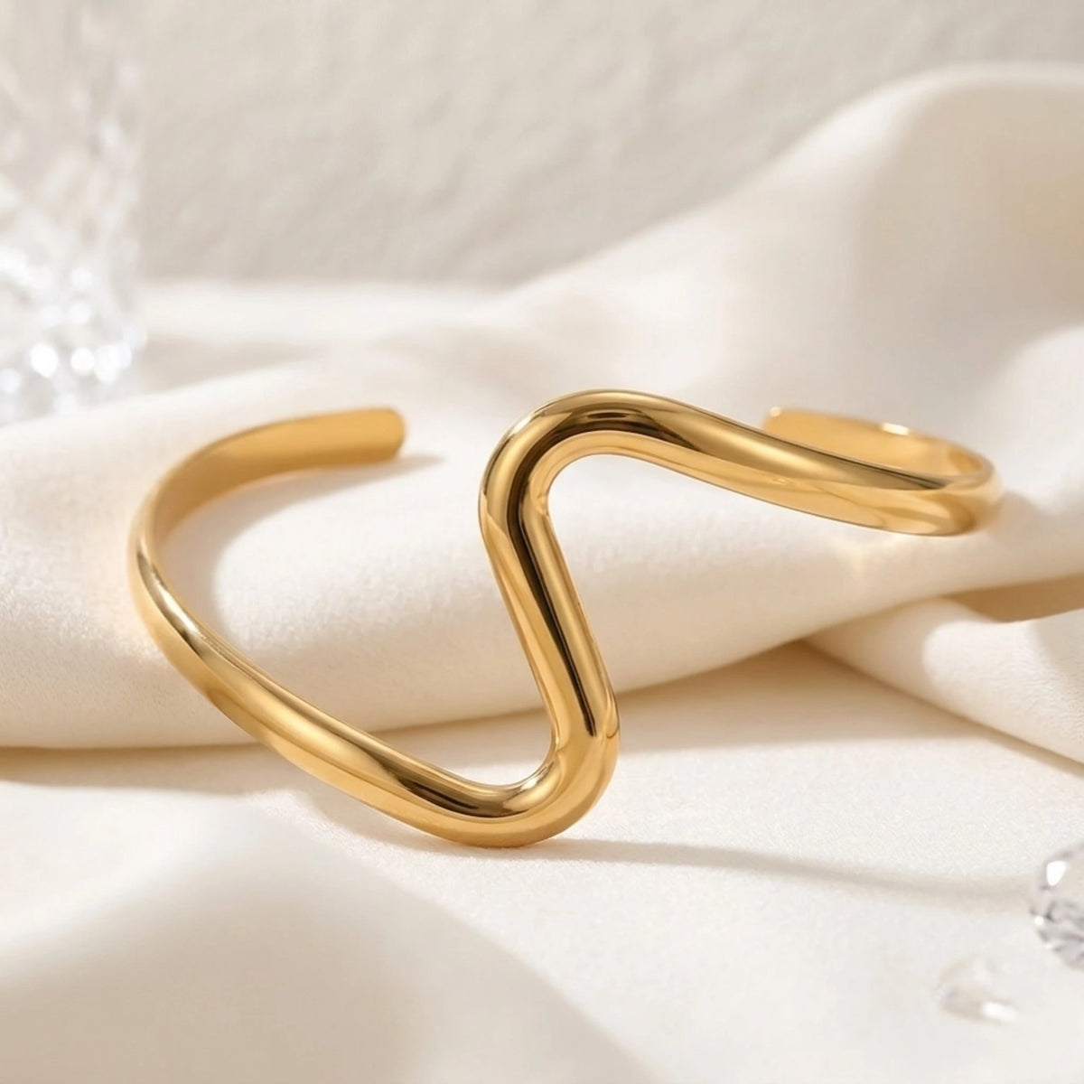 BEHI MILANO Jojo Bracelet — gold S-shaped wave cuff on white decorative surface