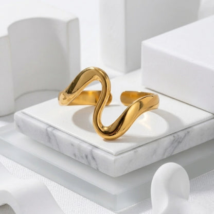 BEHI MILANO Jojo Ring — 18k gold wave ring resting on white marble platform display