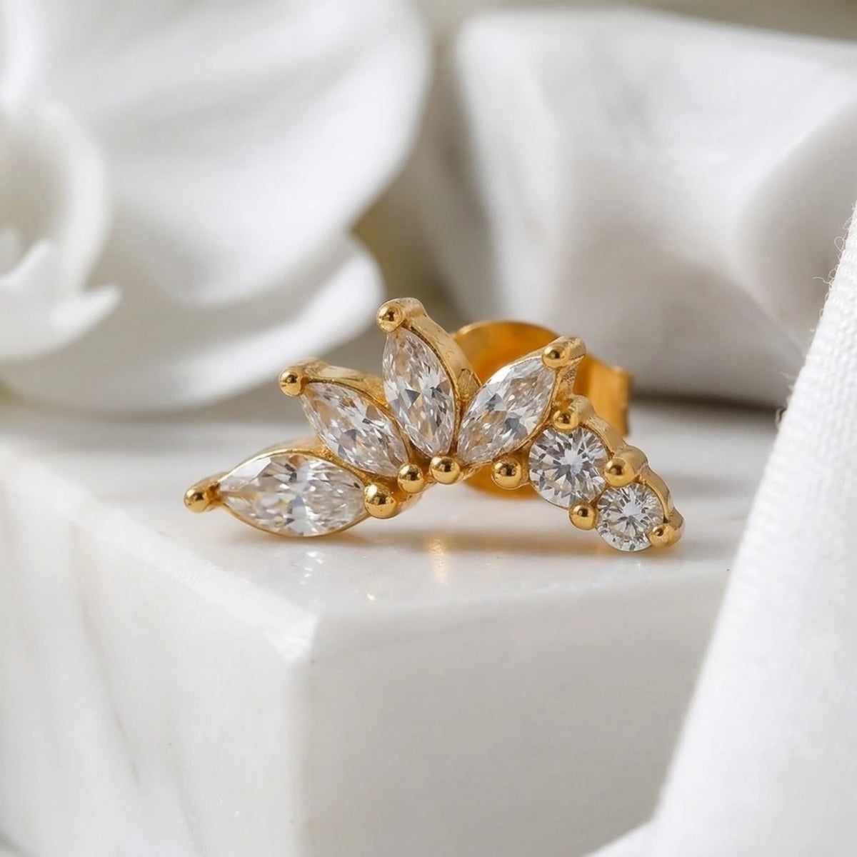 BEHI MILANO Josa Earrings — single gold floral petal crystal stud on white pedestal display