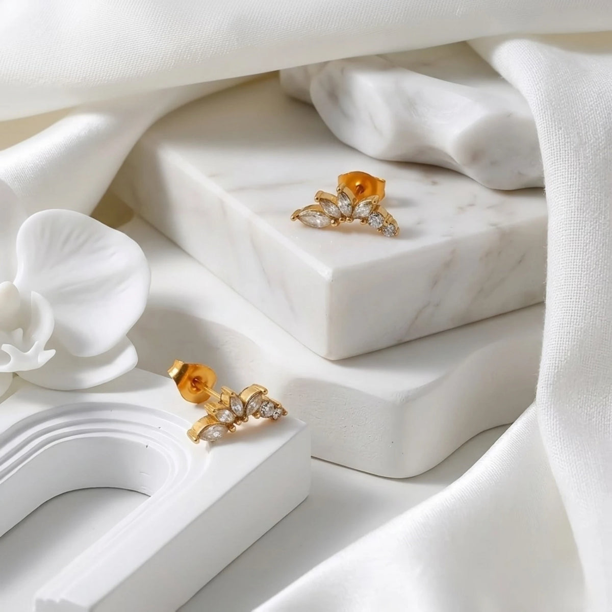 BEHI MILANO Josa Earrings — pair of gold marquise crystal stud earrings on marble surface