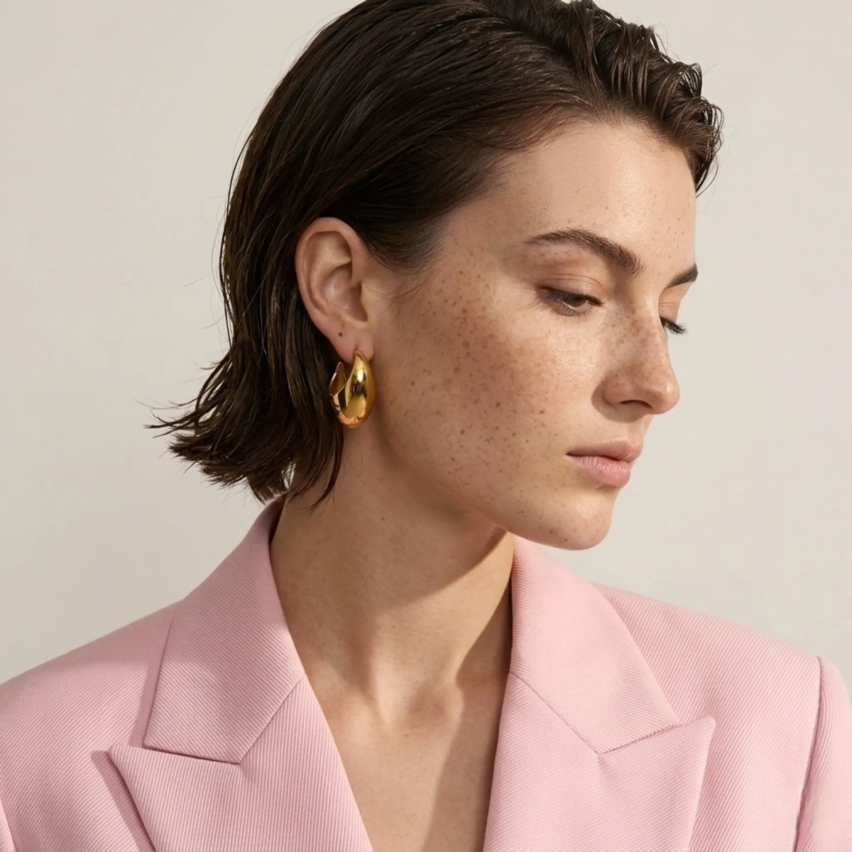 BEHI MILANO Judy Earrings — model wearing pink tailored jacket with gold chunky teardrop hoop earrings