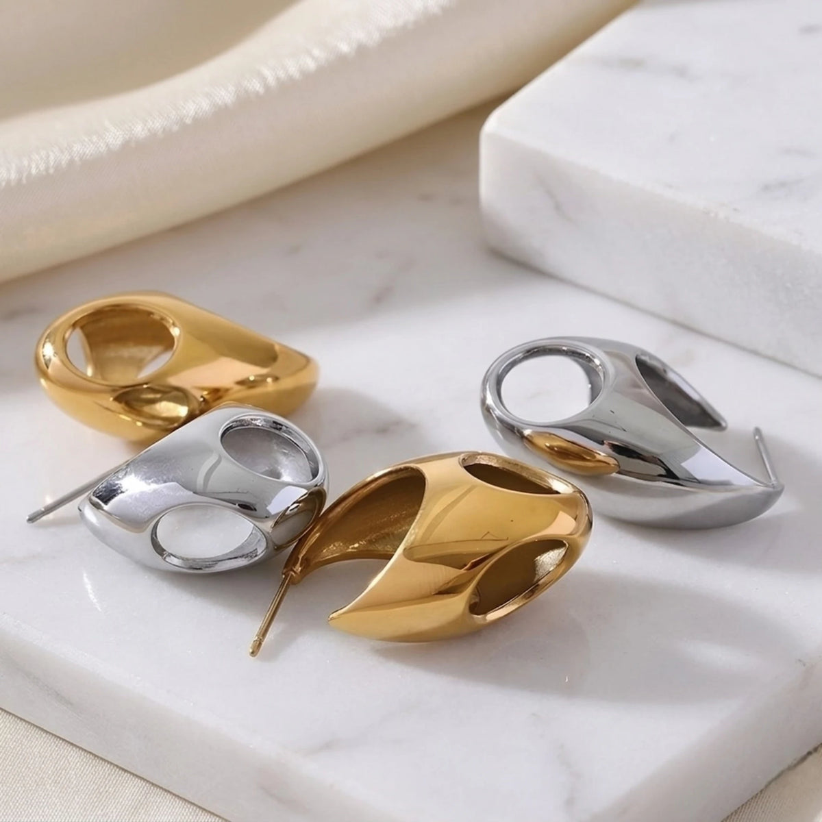 BEHI MILANO Judy Earrings — gold and silver stainless steel chunky teardrop hoop earrings on marble