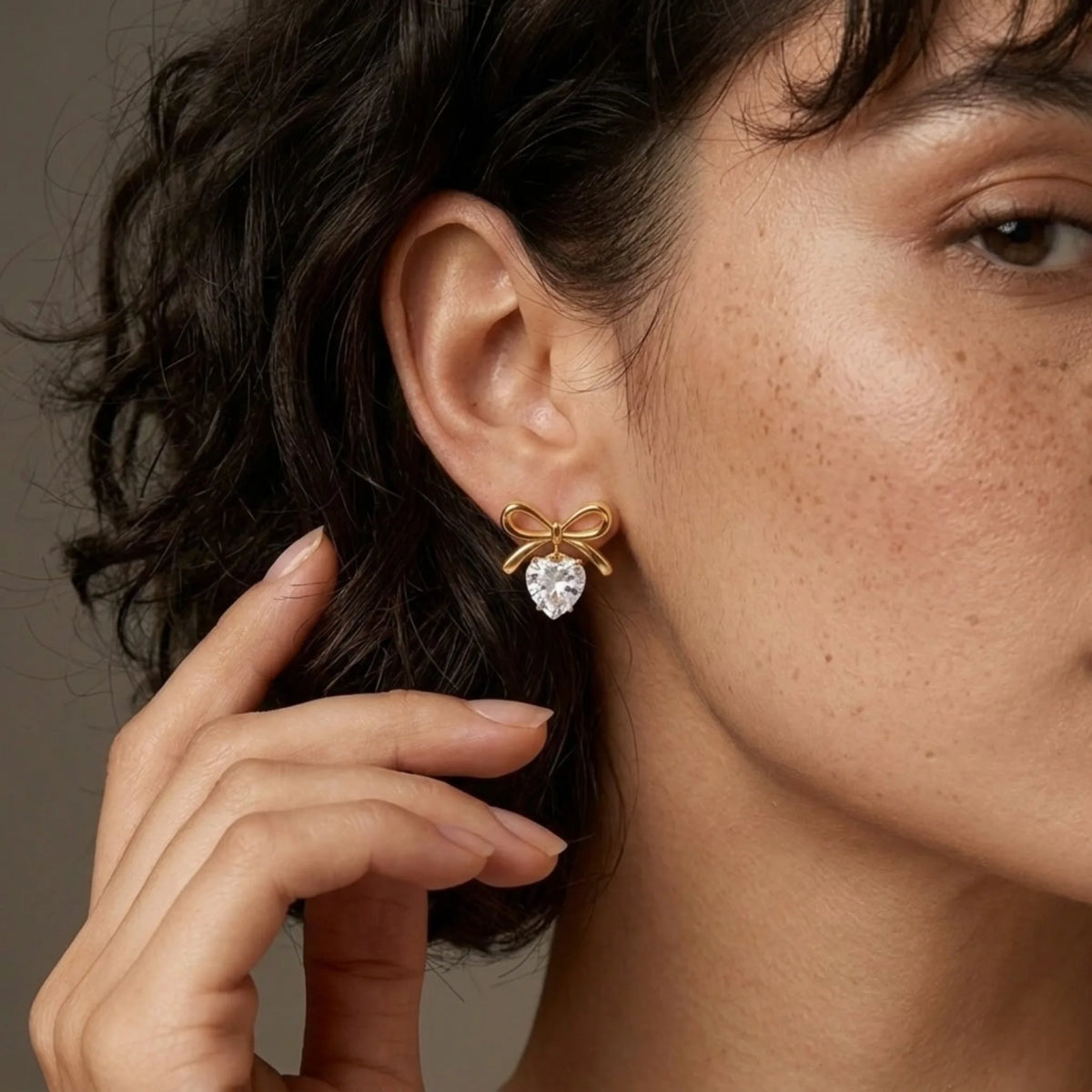 BEHI MILANO Juliette Earrings — close up of gold bow stud with heart-shaped crystal drop on earlobe