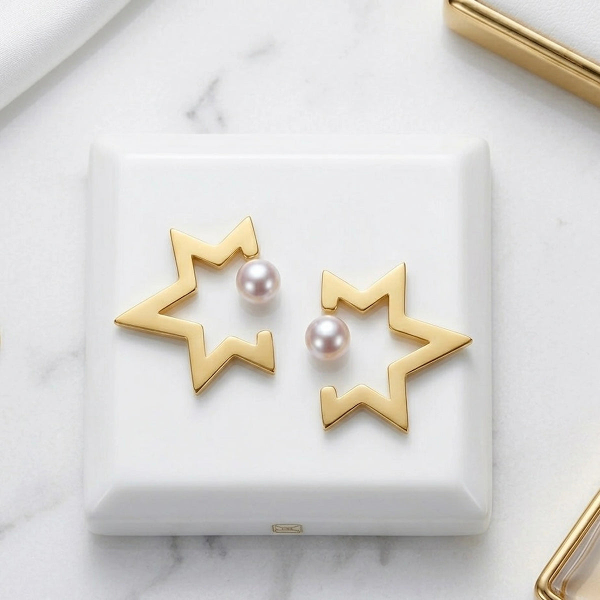 BEHI MILANO Kaia Earrings — pair of gold open star pearl earrings on white marble platform
