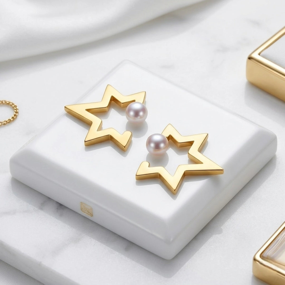 BEHI MILANO Kaia Earrings — 18k gold star pearl studs resting on white ceramic pedestal
