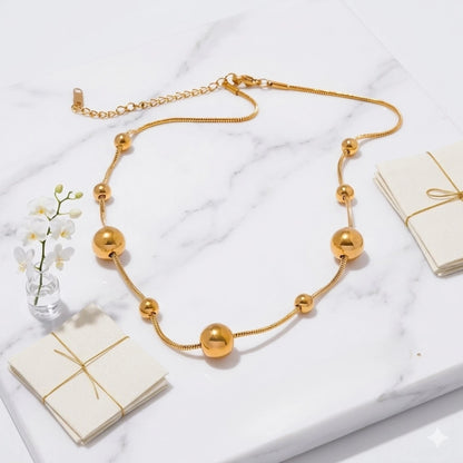 BEHI MILANO Kassia Necklace — gold sphere bead choker displayed on white marble platform