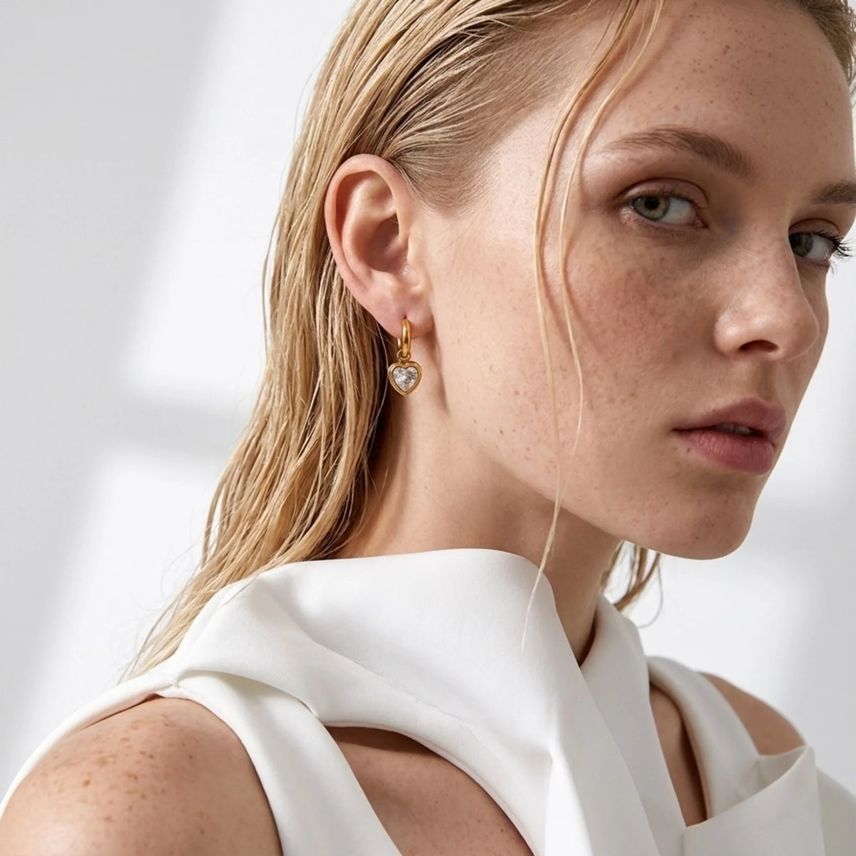 BEHI MILANO Lana Earrings — blonde model wearing gold heart crystal huggie drop earrings