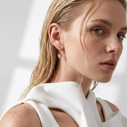 BEHI MILANO Lana Earrings — blonde model wearing gold heart crystal huggie drop earrings