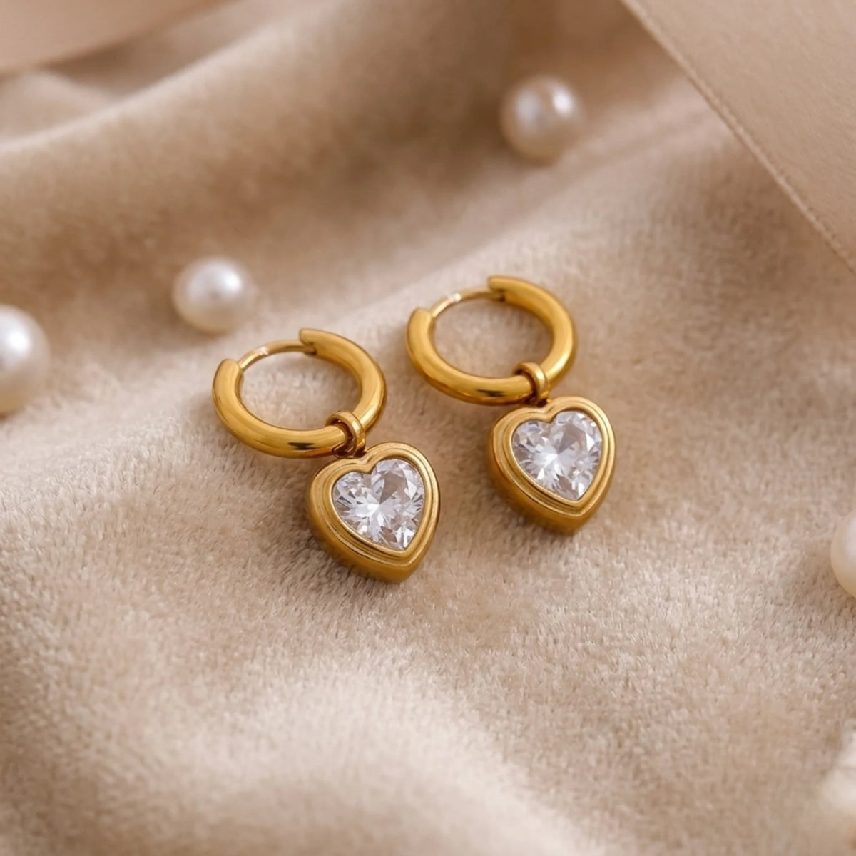BEHI MILANO Lana Earrings — gold heart zircon huggie earrings arranged on draped beige satin with pearls