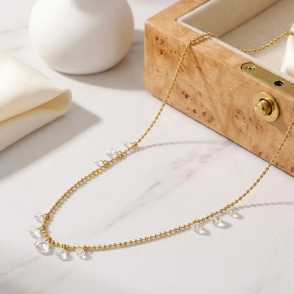 BEHI MILANO Larissa Necklace — gold crystal drop chain flat lay on white pedestal with wooden jewelry box