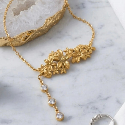 BEHI MILANO Lauris Necklace — gold floral crystal drop necklace arranged on textured decorative surface