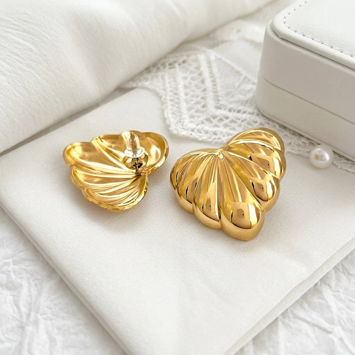 BEHI MILANO Lavina Earrings — gold ribbed leaf studs on textured linen cloth next to gift box