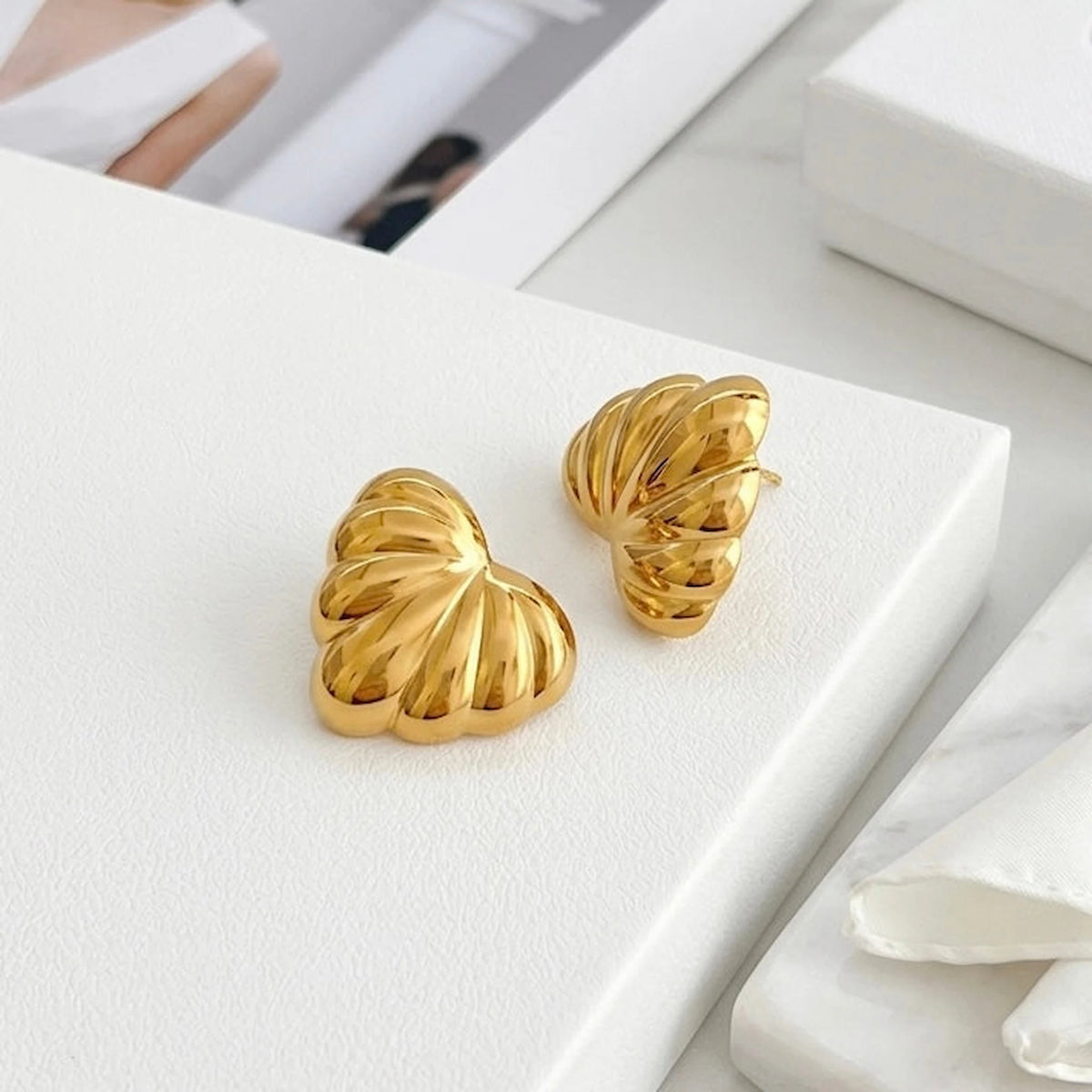 BEHI MILANO Lavina Earrings — gold ribbed leaf studs displayed on tiered white display platform