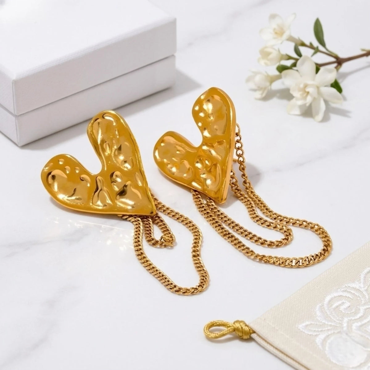 BEHI MILANO Ledda Earrings — gold heart drop earrings styled with white flowers on marble