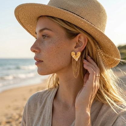BEHI MILANO Ledda Earrings — model wearing gold hammered heart chain drop earrings with sunhat