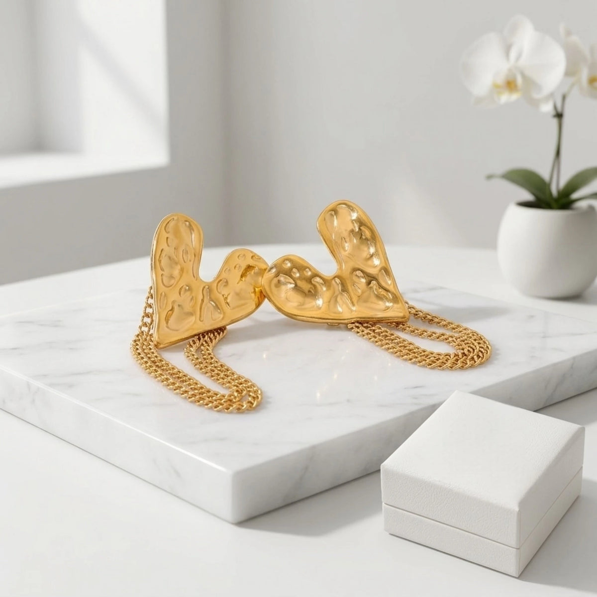 BEHI MILANO Ledda Earrings — gold heart chain statement studs arranged on white display blocks