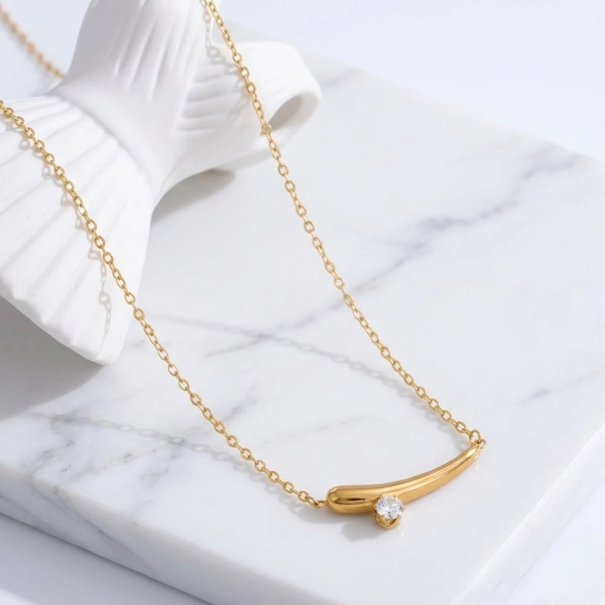 BEHI MILANO Lena Necklace — gold curved horn pendant styled on white marble and linen