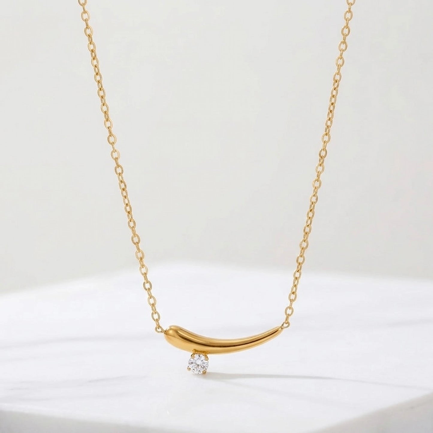 BEHI MILANO Lena Necklace — gold curved zircon pendant hanging shot on white background