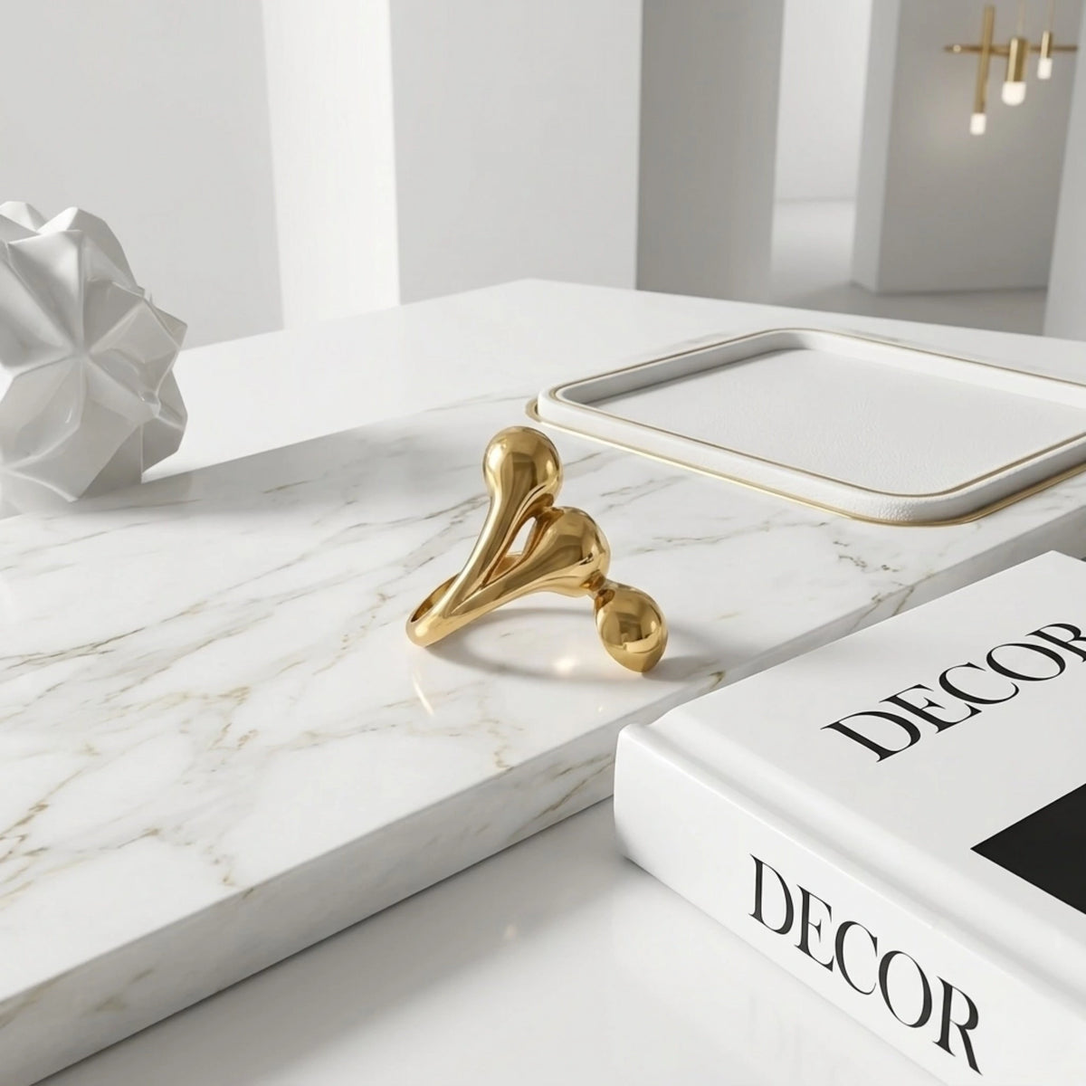 BEHI MILANO Letiz Ring — gold liquid teardrop ring resting on white decor book