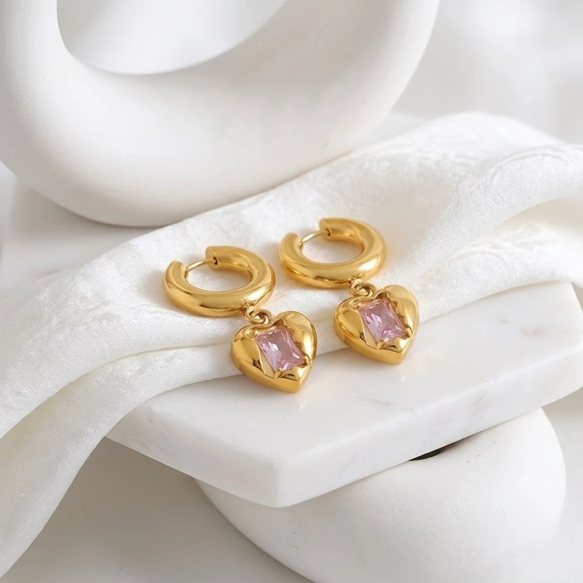 BEHI MILANO Lidia Earrings — gold heart pendant huggie hoops on white studio pedestal